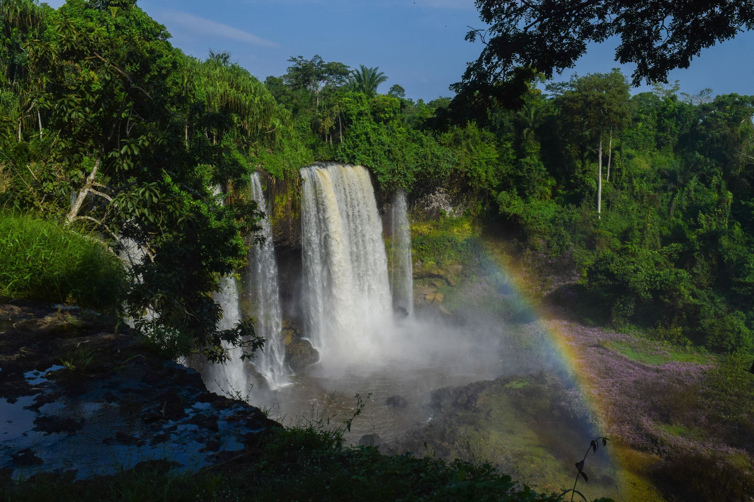 Agbokim Waterfalls pouring into a rainforest gorge, with a rainbow in the spray